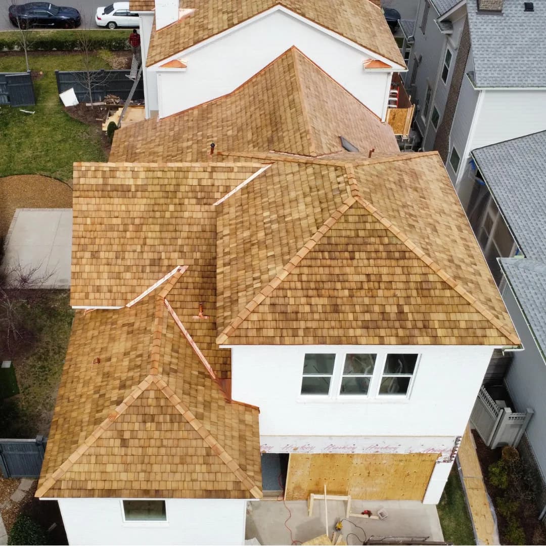 Drone view of a house stripped to bare OSB decking mid-replacement, the surrounding roofs still shingled.