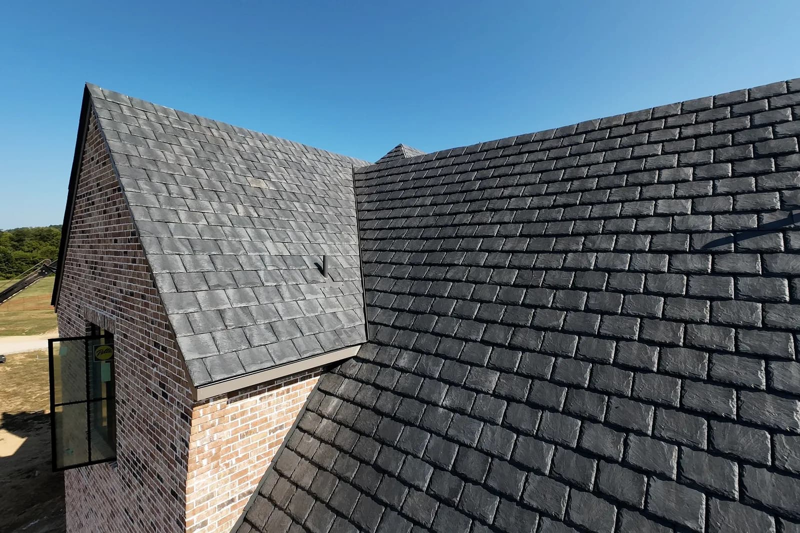 Brava composite slate running to the ridge of a brick gable, the moulded stone texture and the tile-to-tile colour variation in full sun.