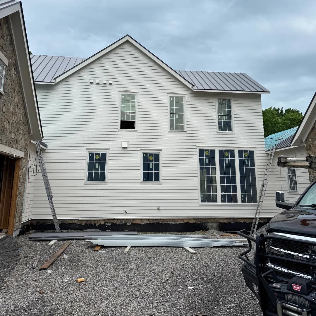 AEM work truck at the curb of a white farmhouse, ladder already set against the eave.