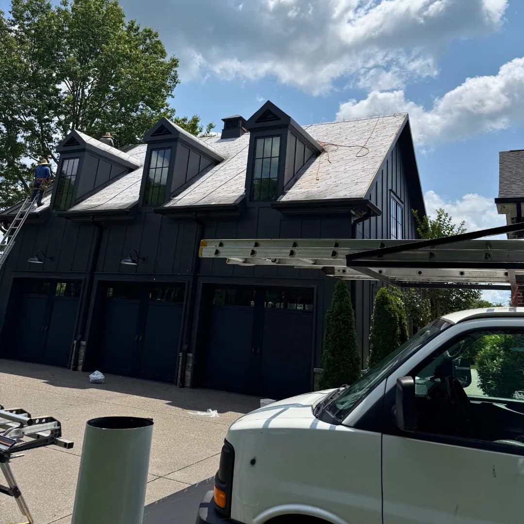Dark metal roof across a run of garage dormers, work van in the drive.
