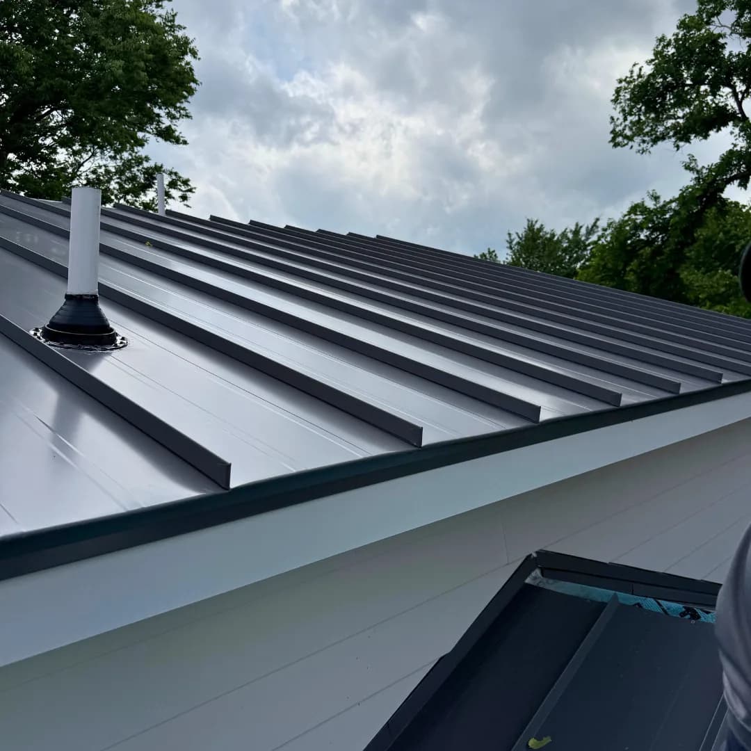Raking light across the raised vertical seams of a standing-seam metal roof, ridge cap running to a skylight.