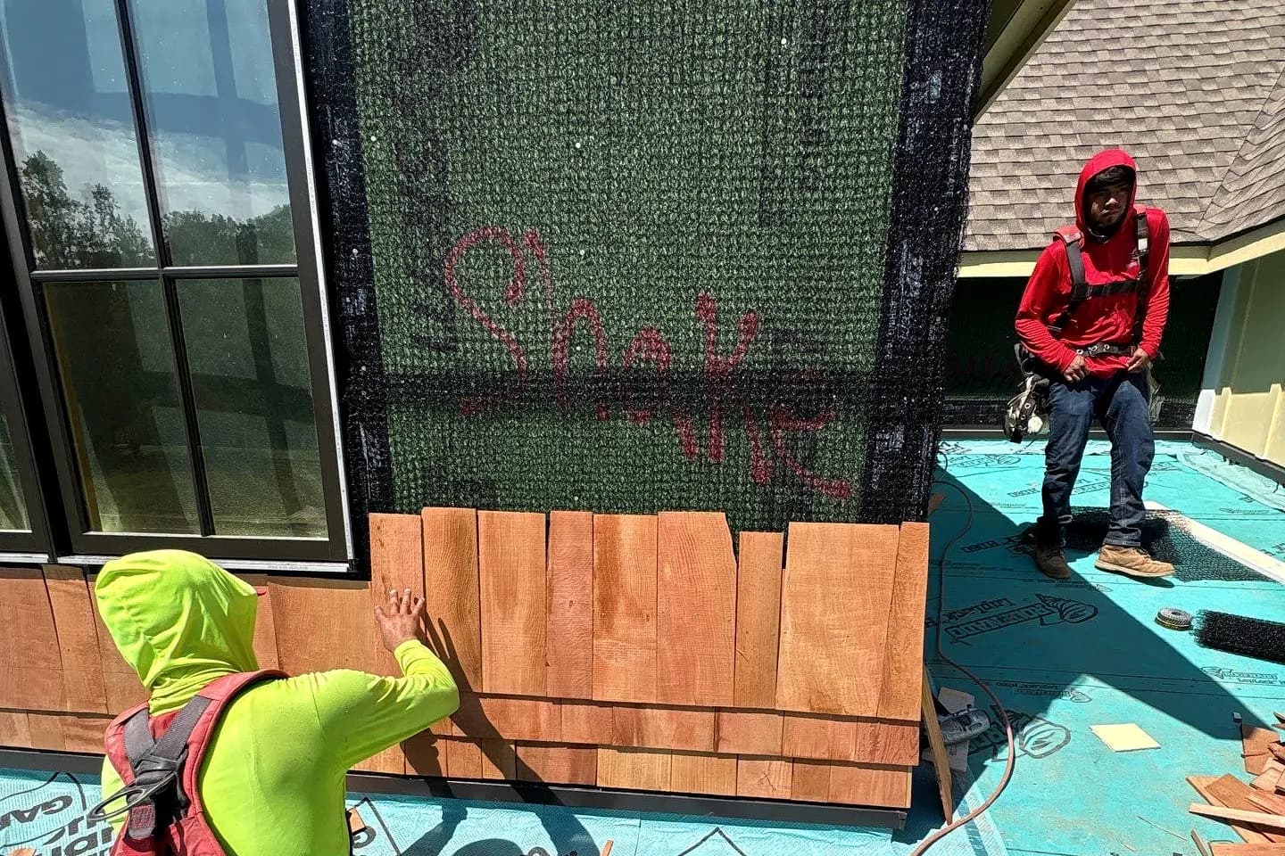 Vertical board-and-batten siding finished on a gable end, the crew working the wrapped elevation beside it from ladders.